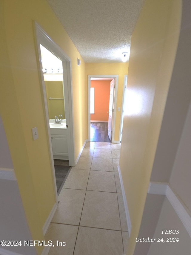 corridor featuring sink, a textured ceiling, and light tile patterned floors