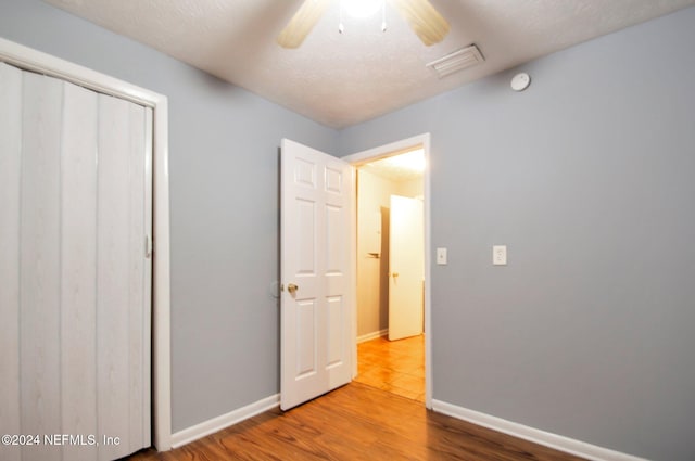 unfurnished bedroom featuring a closet, ceiling fan, wood-type flooring, and a textured ceiling