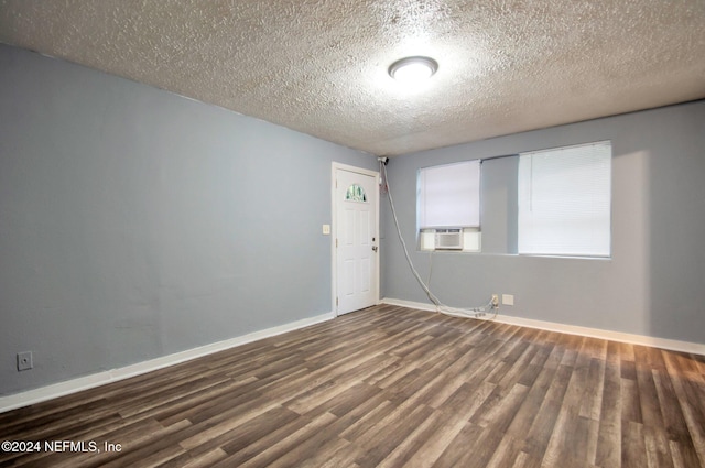 unfurnished room with cooling unit, a textured ceiling, and dark hardwood / wood-style flooring