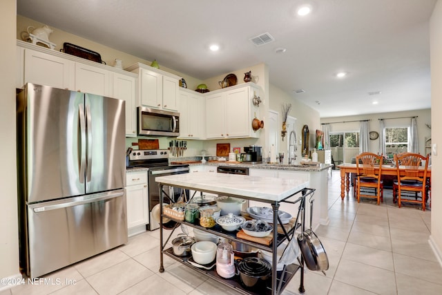 kitchen with kitchen peninsula, light stone counters, light tile patterned flooring, sink, and stainless steel appliances