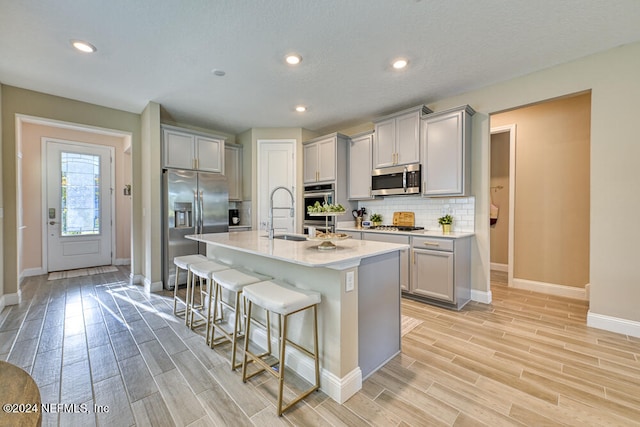 kitchen with stainless steel appliances, light hardwood / wood-style floors, a breakfast bar area, gray cabinets, and a kitchen island with sink