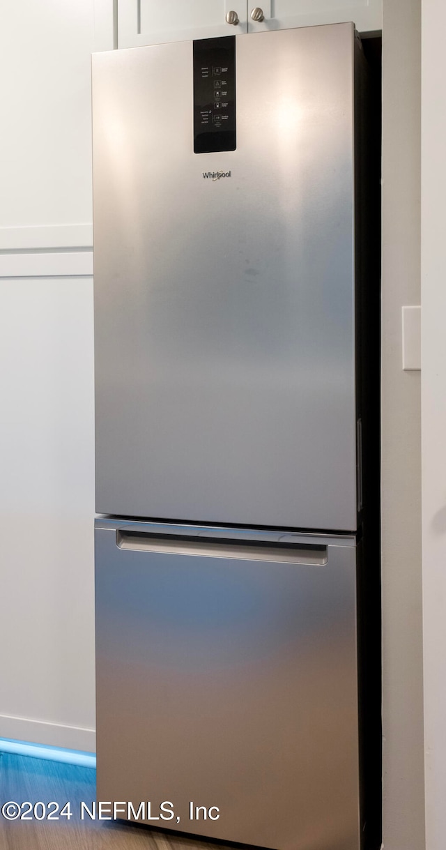 room details with stainless steel fridge, hardwood / wood-style flooring, and white cabinetry