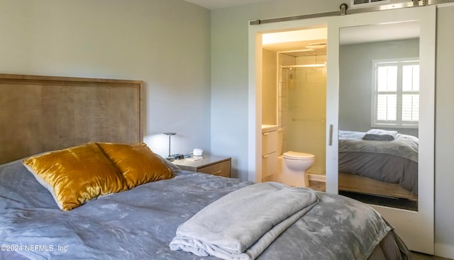 bedroom featuring a walk in closet, a closet, ensuite bath, and a barn door