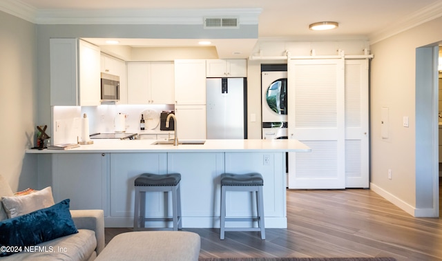 kitchen with white cabinetry, sink, stainless steel appliances, stacked washer / dryer, and kitchen peninsula