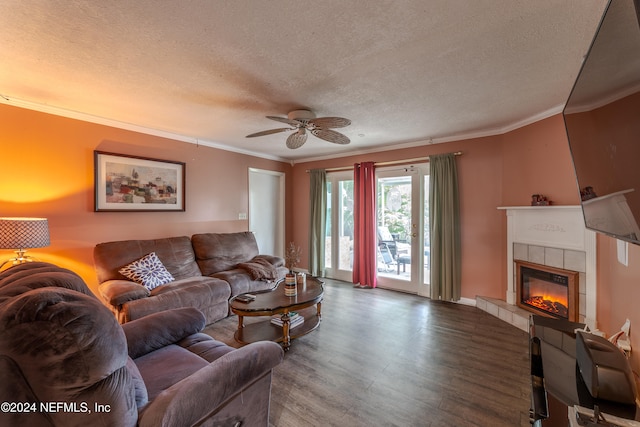 living room featuring wood-type flooring, ornamental molding, a textured ceiling, a tiled fireplace, and ceiling fan