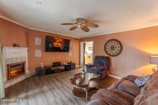 living room featuring a tiled fireplace, ornamental molding, ceiling fan, a textured ceiling, and hardwood / wood-style floors