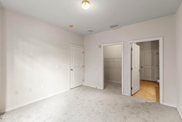 unfurnished bedroom with a spacious closet, light carpet, and a closet