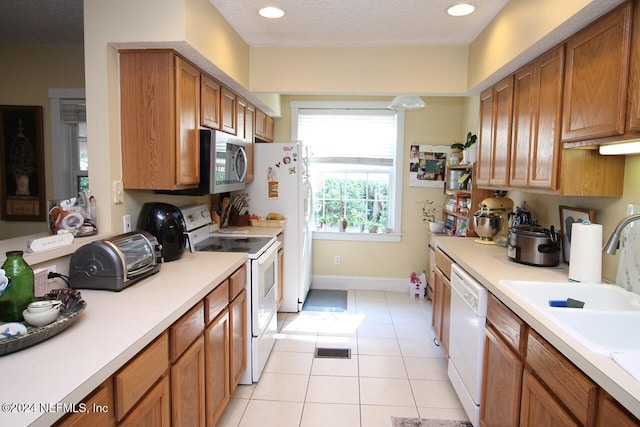 kitchen featuring a textured ceiling, sink, light tile patterned floors, and white appliances