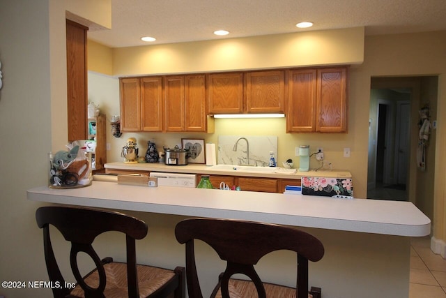 kitchen featuring dishwasher, kitchen peninsula, sink, light tile patterned flooring, and a textured ceiling