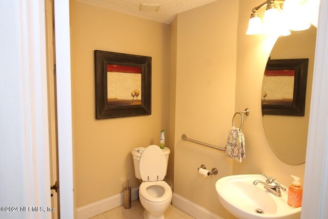 bathroom with toilet, a textured ceiling, sink, and tile patterned flooring