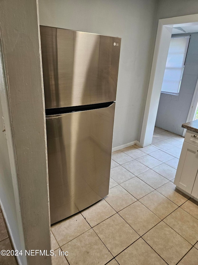 kitchen with stainless steel fridge, light tile patterned floors, and white cabinets