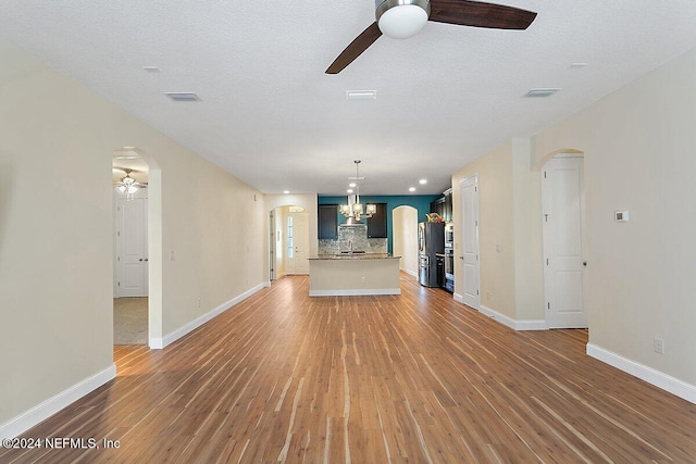 unfurnished living room featuring a textured ceiling, wood-type flooring, and ceiling fan with notable chandelier