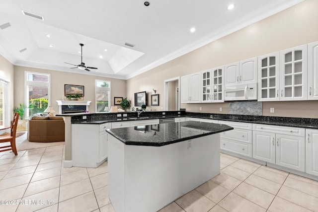 kitchen with a tray ceiling, white cabinets, dark stone countertops, kitchen peninsula, and a center island