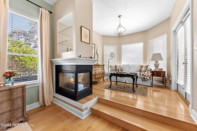 living area with a chandelier, a multi sided fireplace, hardwood / wood-style flooring, and a healthy amount of sunlight