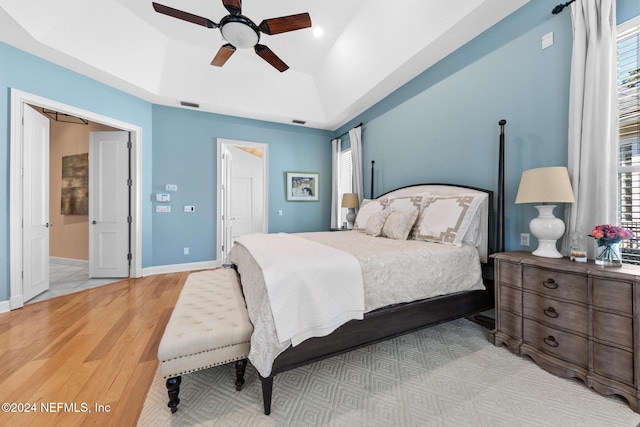 bedroom featuring ceiling fan, multiple windows, light wood-type flooring, and a tray ceiling