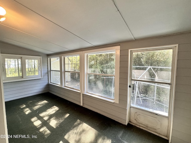 unfurnished sunroom with carpet flooring, wood walls, a healthy amount of sunlight, and lofted ceiling