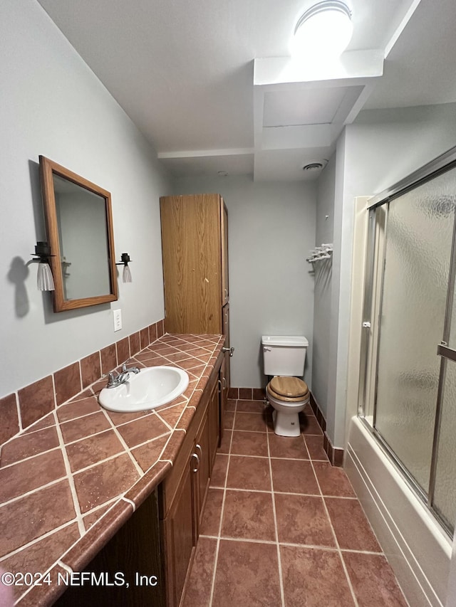 bathroom with toilet, baseboards, shower / bath combination with glass door, and vanity