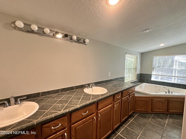 full bath featuring a textured ceiling, a tub with jets, a sink, and tile patterned floors