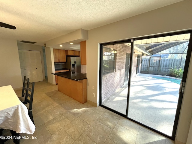 kitchen featuring stainless steel fridge, a textured ceiling, light tile patterned floors, and backsplash