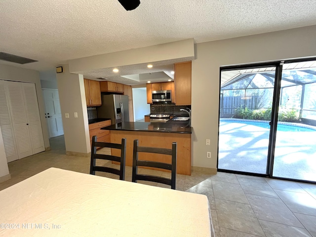 kitchen with tasteful backsplash, appliances with stainless steel finishes, a textured ceiling, light tile patterned flooring, and sink