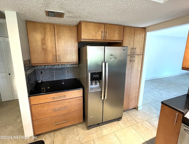 kitchen featuring backsplash, a textured ceiling, stainless steel fridge, dark stone counters, and light tile patterned floors