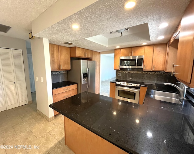 kitchen featuring tasteful backsplash, a raised ceiling, appliances with stainless steel finishes, a textured ceiling, and sink