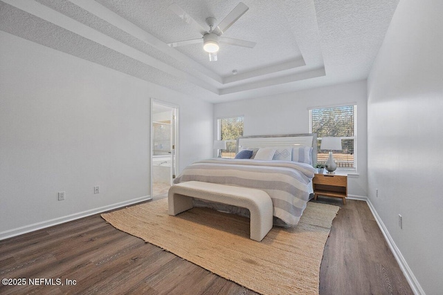 bedroom with dark wood-type flooring, ensuite bathroom, a textured ceiling, a tray ceiling, and ceiling fan