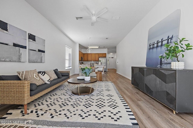 living room with ceiling fan, a textured ceiling, and light hardwood / wood-style flooring