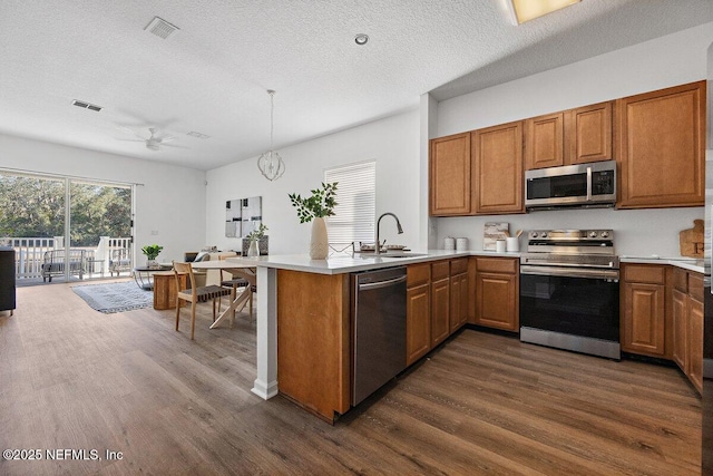 kitchen with appliances with stainless steel finishes, dark hardwood / wood-style floors, sink, kitchen peninsula, and a textured ceiling