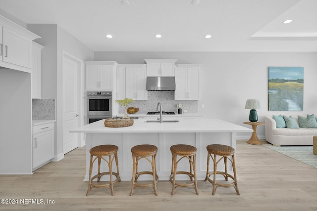 kitchen featuring tasteful backsplash, a kitchen island with sink, light hardwood / wood-style flooring, and white cabinetry