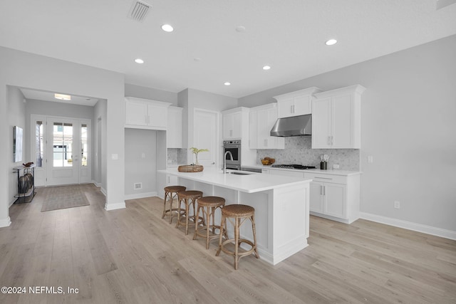 kitchen with a kitchen breakfast bar, light wood-type flooring, stainless steel gas cooktop, white cabinetry, and an island with sink