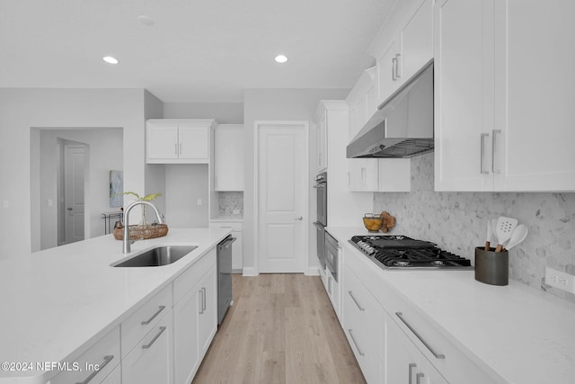 kitchen with light wood-type flooring, tasteful backsplash, stainless steel appliances, sink, and white cabinetry