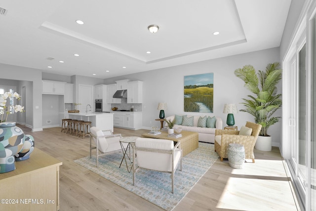 living room featuring a tray ceiling, sink, and light hardwood / wood-style flooring