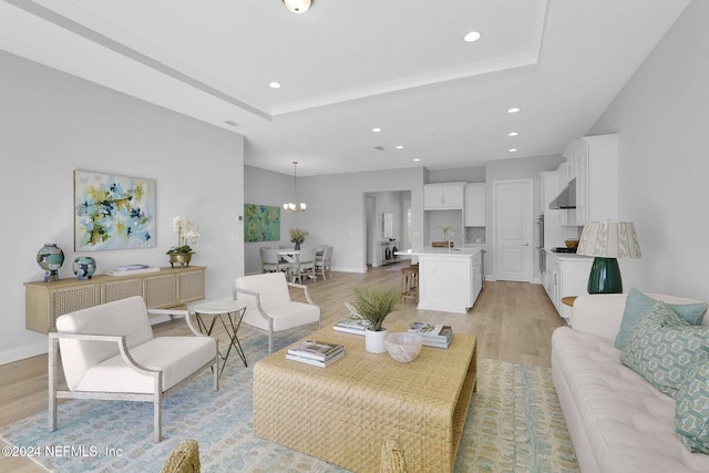 living room featuring a raised ceiling, sink, a notable chandelier, and light wood-type flooring