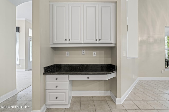 kitchen featuring dark stone counters, white cabinetry, built in desk, and light tile patterned floors