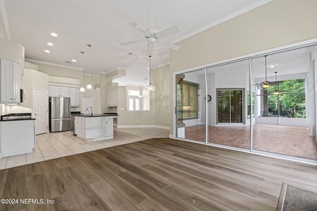 kitchen with white cabinets, light wood-type flooring, decorative light fixtures, and stainless steel fridge