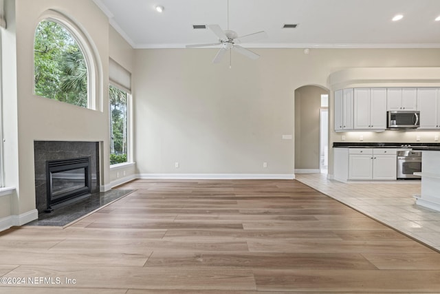 unfurnished living room with ornamental molding, a premium fireplace, light hardwood / wood-style flooring, and ceiling fan