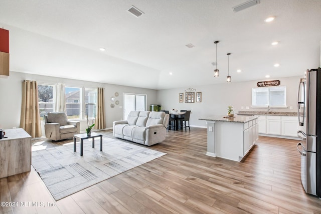 living room featuring sink, light wood-type flooring, and vaulted ceiling