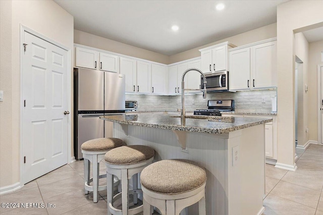 kitchen with white cabinetry, stainless steel appliances, and an island with sink