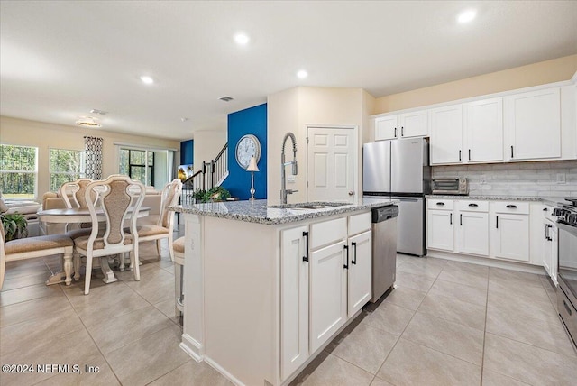 kitchen with appliances with stainless steel finishes, sink, an island with sink, white cabinets, and light stone counters