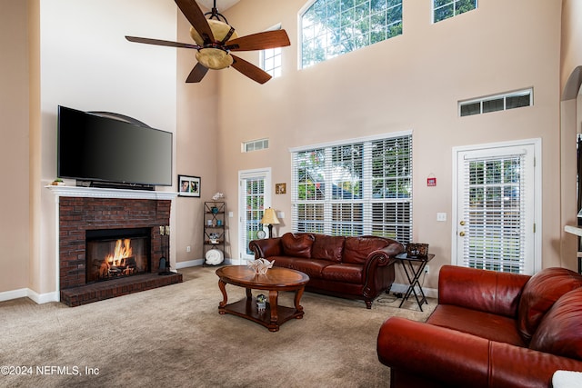 carpeted living room with a wealth of natural light, a fireplace, a towering ceiling, and ceiling fan