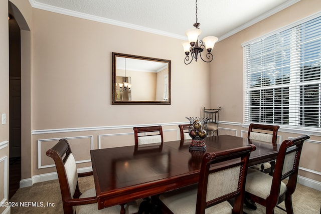 carpeted dining space with a textured ceiling, ornamental molding, and an inviting chandelier