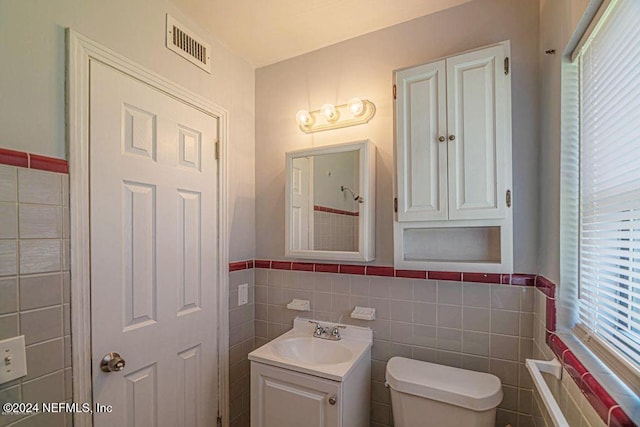 bathroom featuring vanity, toilet, a healthy amount of sunlight, and tile walls