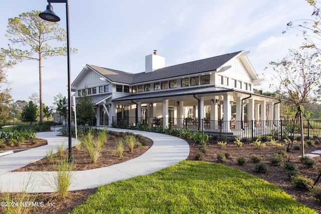back of property with a chimney, a standing seam roof, fence, metal roof, and roof with shingles