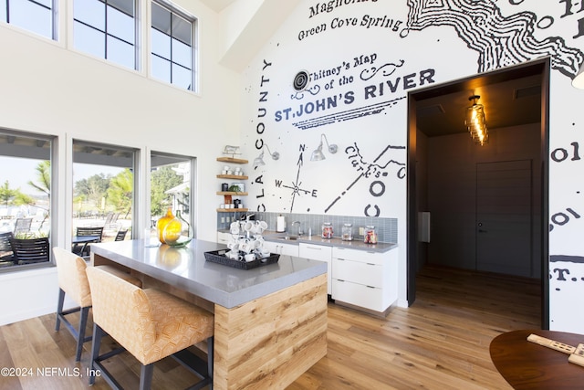kitchen with white cabinets, a sink, a kitchen island, light wood-type flooring, and a towering ceiling