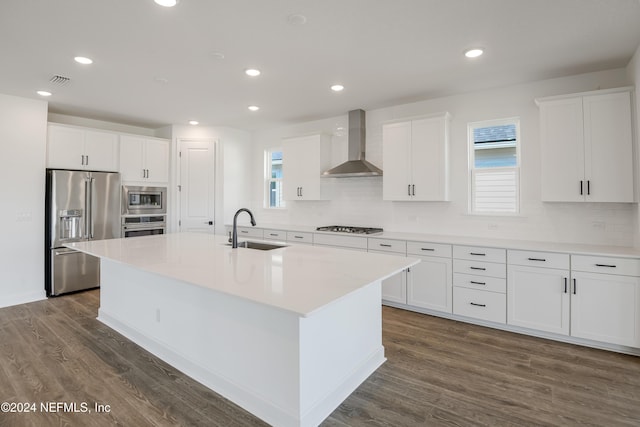 kitchen with stainless steel appliances, a kitchen island with sink, sink, wall chimney range hood, and white cabinets