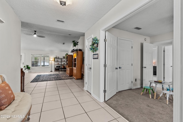 hallway featuring a textured ceiling, light tile patterned floors, and vaulted ceiling