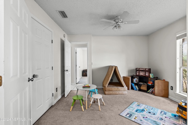 recreation room featuring ceiling fan, a textured ceiling, and carpet floors