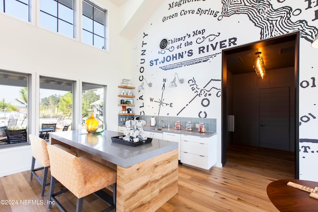 kitchen with decorative backsplash, white cabinetry, light wood-type flooring, a towering ceiling, and sink