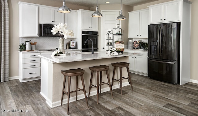 kitchen with a center island with sink, black appliances, white cabinets, and pendant lighting